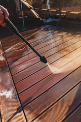 man cleaning terrace with a power washer - high water pressure cleaner on wooden terrace surface