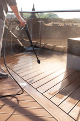 man cleaning terrace with a power washer - high water pressure cleaner on wooden terrace surface