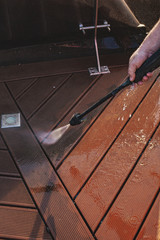 man cleaning terrace with a power washer - high water pressure cleaner on wooden terrace surface