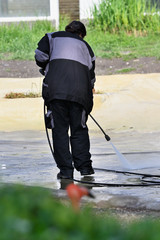 Woman splashing water pressure gun on concrete.