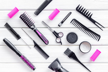 Combs, sciccors and pink hairdresser tools in beauty salon work desk on white wooden background top view pattern