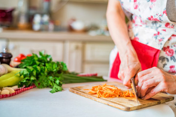 Female hand with knife chops carrot in kitchen. Cooking vegetables