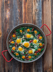 Fried eggs with spinach and pine nuts in iron skillet, copy space