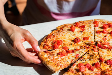 People's hands taking slices of fresh pizza Margherita with tomatoes