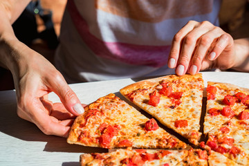 People's hands taking slices of fresh pizza Margherita with tomatoes
