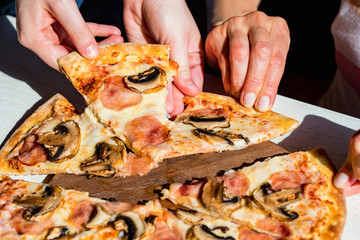 Hands take slices of fresh pizza with salami, mushrooms and cheese close up