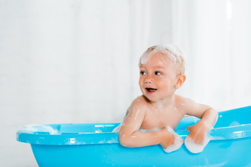 naked and cute toddler kid smiling while taking bath in plastic baby bathtub