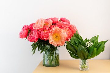 Coral peonies and spring lilies of the valley in a glass vase on wooden table.. Beautiful peony flower for catalog or online store. Floral shop concept . Beautiful fresh cut bouquet. Flowers delivery.