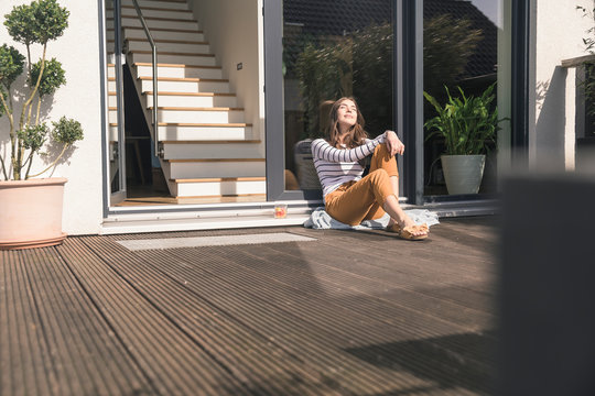 Young woman sitting on terrace at home enjoying the sunshine