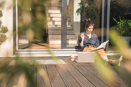Young woman sitting on terrace at home working with book and laptop