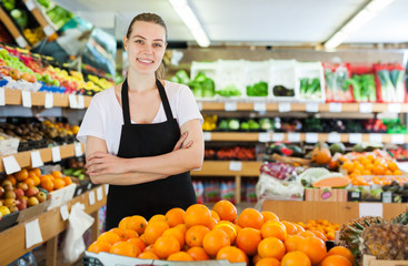 Smiling woman seller wearing apron standing near fresh oranges