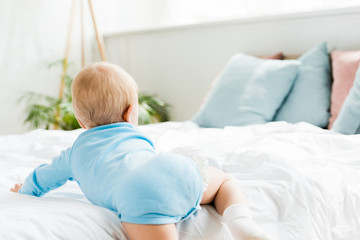 back view of toddler child crawling on bed in modern bedroom