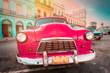Poster Antique pink car inext to colorful buildings in Old Havana © kmiragaya