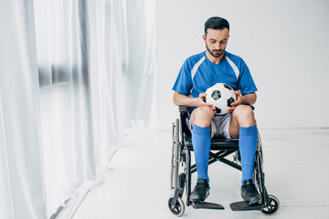man in football uniform sitting in Wheelchair and holding soccer ball