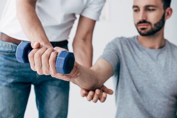 chiropractor stretching arm of patient with dumbbell on grey