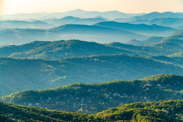 Fototapeta premium Layers of mountains in the haze during sunset. Beautiful sunset in the mountains. Beautiful sunset in a hilly valley with villages and fog in the lowlands.