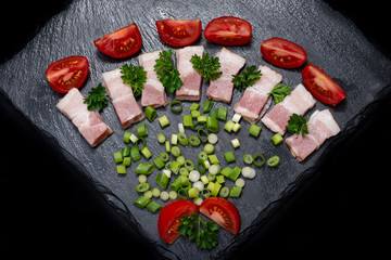 Uncured Apple Smoked Bacon, Red Tomatoes, fresh Curly Parsley and Green Onion Scallions arranged on natural black stone background. 