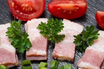 Uncured Apple Smoked Bacon, Red Tomatoes, fresh Curly Parsley and Green Onion Scallions arranged on natural black stone background. 
