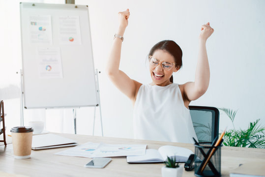 excited businesswoman celebrating triumph while sitting at workplace in office