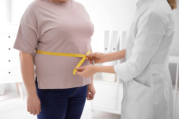 Doctor measuring waist of overweight woman in clinic, closeup - obrazy, fototapety, plakaty