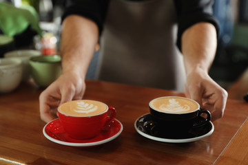 Barista putting cups of coffee on wooden table, closeup. Space for text