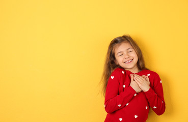 Portrait of girl holding hands near her heart on color background. Space for text