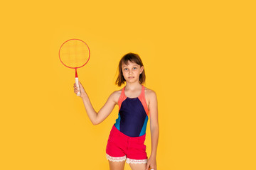 Portrait of young female player in blue t-shirt playing badminton on yellow background