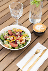 Fresh raw vegetarian salad of spinach leaves with quinoa and chia seeds. Juicy grapefruit, red pomegranate and sweet pomelo. In a deep plate with golden cutlery and cup coffee. Glass water, breakfast.