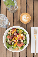 Fresh raw vegetarian salad of spinach leaves with quinoa and chia seeds. Juicy grapefruit, red pomegranate and sweet pomelo. In a deep plate with golden cutlery and cup coffee. Glass water, breakfast.