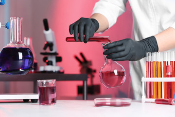 Scientist pouring reagent into flask at table in chemistry laboratory