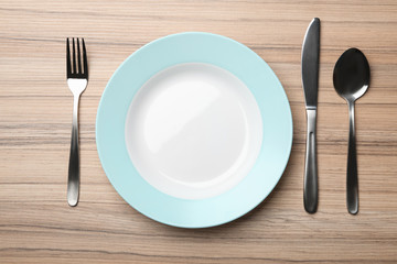 Stylish ceramic plate and cutlery on wooden background, flat lay