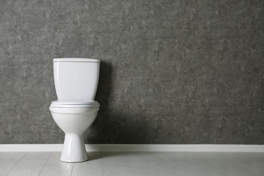 New toilet bowl near grey wall indoors. Space for text