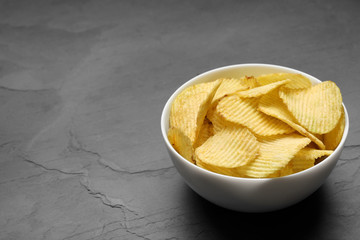 Bowl of potato chips on grey table. Space for text