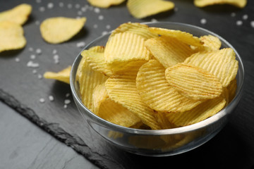 Slate board with bowl of potato chips on grey table, closeup. Space for text