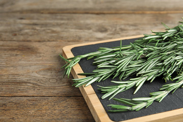 Board with fresh rosemary twigs on wooden table, closeup. Space for text