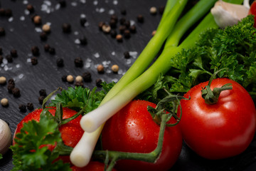 Organic Red Tomatoes on the vine, Curly Parsley, Green Scallions, Garlic, Rainbow Peppercorns and Sea Salt arranged on natural stone background. 