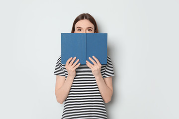 Young woman hiding behind book on white background, space for text. Reading activity