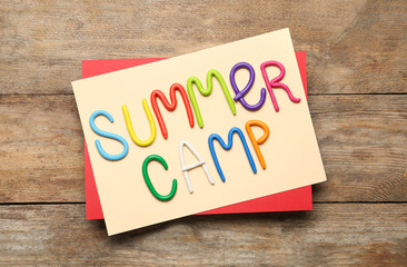 Text SUMMER CAMP made of modelling clay on wooden table, flat lay