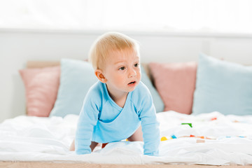 surprised toddler child crawling on bed with white bedding at home