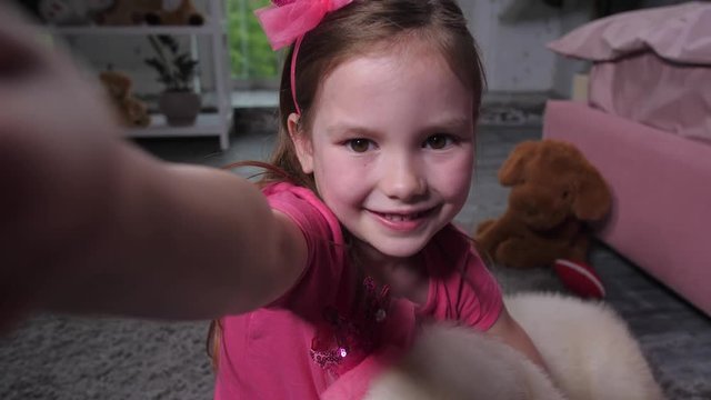 Close-up portrait of smiling elementary age girl with cellphone posing for selfie shot sitting on floor and hugging golden retriever pet. Cute child taking selfie photo with fluffy puppy in nursery