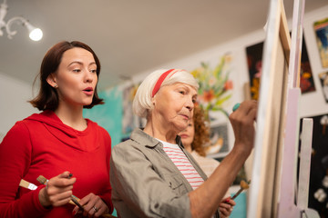 Dark-haired student watching her aged teacher painting