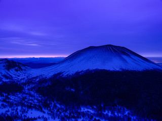 Fototapeta premium 峠から雪山を撮影、空は濃いブルー色の雲に覆われ遠くの地平線がほんのり朝焼け色に染まる、この山の特有な筋状の残雪模様が目を引く。