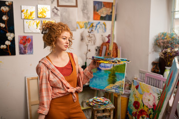Curly young artist feeling thoughtful while working on new picture