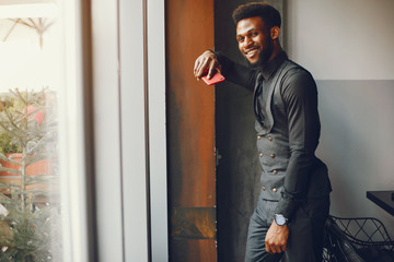 A young and handsome dark-skinned boy in a black suit standing in a cafe