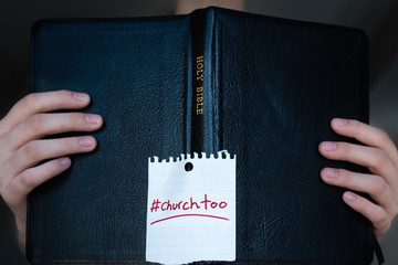 Woman holding Holy Bible with #churchtoo hashtag written on cover