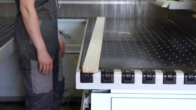 Worker man receives a piece of laminated chipboard at a format-raskroyechny center with numerical program control at a furniture manufacturing factory