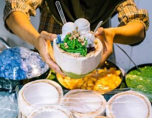 Coconut ice cream with some snack in coconut holding by seller's hands. Thai favourite street food.