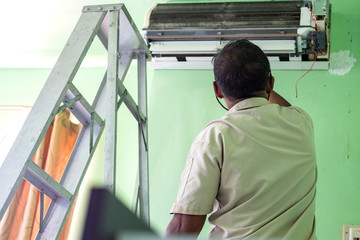 Workers repairs and cleans the air conditioner in the room. Steel ladder used by the worker to climb up to close to the air conditioner.