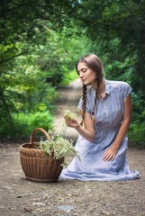 Gorgeous girl with piggy tails in blue floral dress sitting in the middle of the road with her basket full with flowers