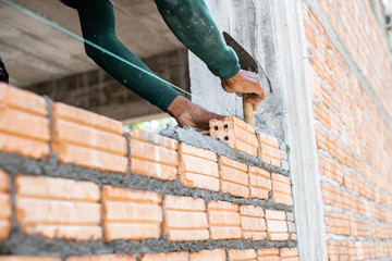 Close up of bricklayer worker's hand installing red brick with trowel putty knife for new house building at construction site.